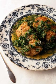 a blue and white plate topped with meat covered in greens