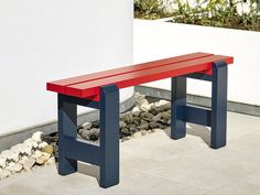 a red and blue bench sitting next to a white wall on top of a stone floor