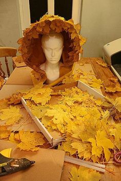 a table topped with lots of yellow leaves and a head in a paper bag on top of it