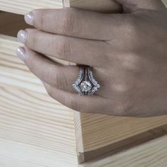 a woman's hand holding an engagement ring on top of a piece of wood