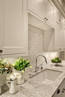 a kitchen with marble counter tops and white cabinets, along with two vases filled with flowers