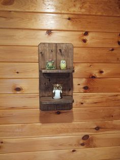 two owl figurines sitting on top of a shelf in a wooden room with wood paneling