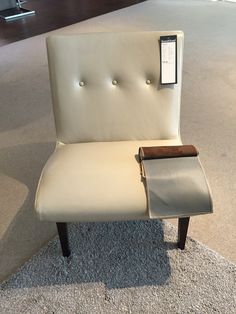 a white chair with a wooden arm rest on carpeted area next to wall and window