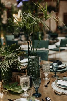 the table is set with plates, silverware and palm trees in vases on it