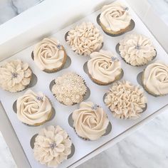 twelve cupcakes with white frosting in a box on a marble countertop