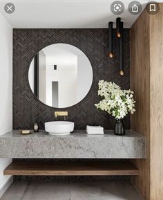 a bathroom with marble counter tops and a round mirror on the wall, along with two vases filled with flowers