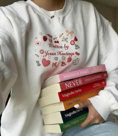 a person sitting down holding four books in their hands and wearing a white sweatshirt with the words written on it