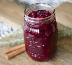 a jar filled with cranberry sauce next to cinnamon sticks