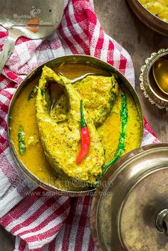 a metal bowl filled with yellow curry next to two silver dishes on a red and white checkered towel