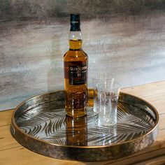 a bottle of whisky sitting on top of a metal tray next to two shot glasses