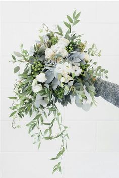 a bridal bouquet with white flowers and greenery is being held by someone's hand