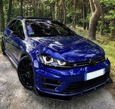 a blue car parked on the side of a road in front of trees and grass