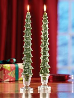 two candles are sitting next to each other on a table with presents in the background