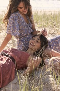 two women are laying on the beach and one is combing her hair while the other looks at her