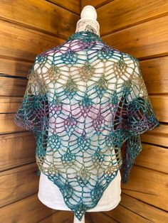 a crocheted shawl hanging on a mannequin's dummy in front of a wooden wall