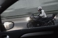 a man riding on the back of a motorcycle next to a car in front of him