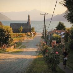 a person riding a bike down a dirt road next to the ocean with mountains in the background