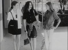 three young women are walking down the sidewalk in front of a building and talking to each other