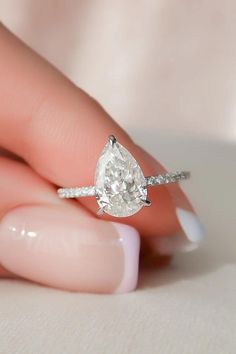 a woman's hand holding an engagement ring with a pear shaped diamond on it