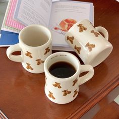 two mugs with coffee sit next to an open book