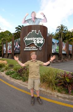 a young boy standing in front of a sign for australia zoo with his hands up