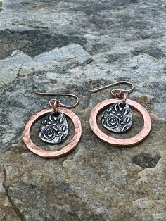 two circular earrings with an image of a cat in the center on top of a rock