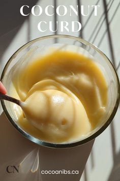 a spoon in a glass bowl filled with cream and honey sauce on a white table