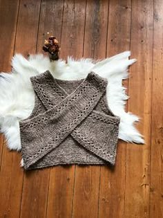 a knitted vest laying on top of a wooden floor next to a teddy bear