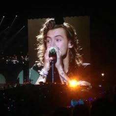 a man with long hair holding a microphone in front of a crowd at a concert