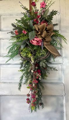 a wreath hanging on the side of a door with flowers and greenery attached to it