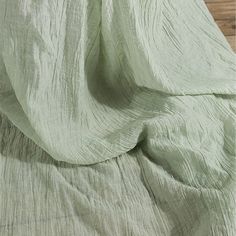 an unmade bed with green sheets on top of it and wood flooring in the background