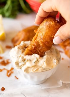 a person dipping some food into a small white bowl filled with dip and sauce on the side