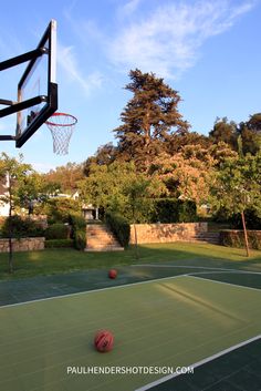 an outdoor basketball court with a basket and ball in the air, surrounded by trees