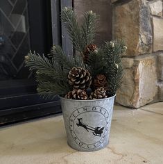 a metal bucket filled with pine cones and evergreen branches sitting on top of a stone floor