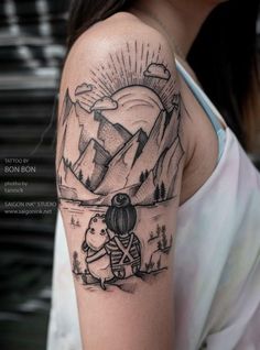 a woman with a tattoo on her arm is standing in front of a mountain range