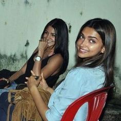 two young women sitting next to each other on a red chair in front of a wall