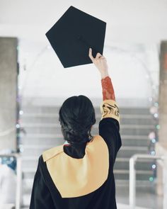 a woman holding up a black graduation cap