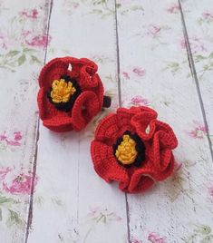 two crocheted red flowers sitting on top of a white table next to each other