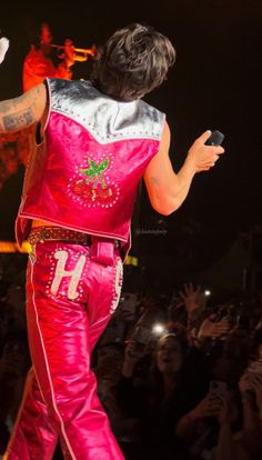 a man in a pink outfit on stage with his arms out to the side as he sings