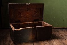 an old wooden box sitting on top of a wooden floor next to a green wall