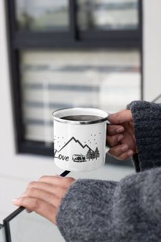 a person holding a coffee cup with the words love on it and mountains in the background