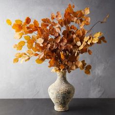 a vase filled with lots of leaves on top of a table next to a wall