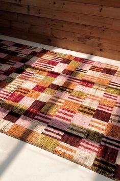 a multicolored patchwork rug on the floor in front of a wooden wall