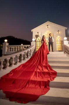 a woman in a red dress standing on some steps next to a man wearing a suit