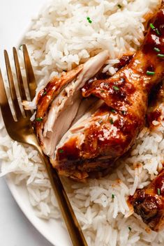 a white plate topped with rice and meat covered in sauce next to a golden fork