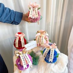 four small pom poms with ribbons and name tags on them sitting on a table