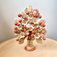 a ceramic figurine with flowers and leaves on top of a wooden table in front of a white wall