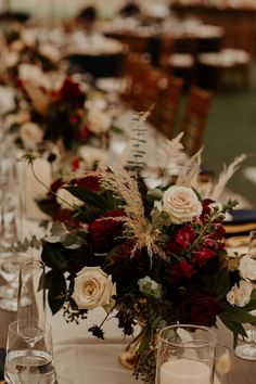 the table is set with white and red flowers, greenery, candles and wine glasses