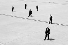 black and white photograph of men in suits walking across an airport tarmac with no one on it