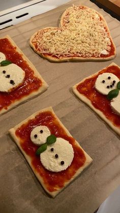 four pizzas with faces on them sitting on top of a baking sheet in the shape of hearts